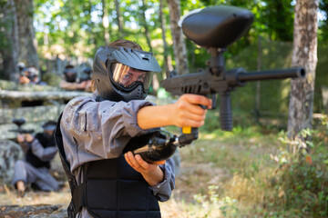 Woman targeting with paintball gun to eliminate enemies on battlefield. Markswoman shooting with paintball marker.