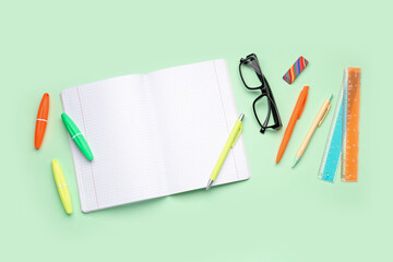 Blank copybook pages, glasses and stationery on green background