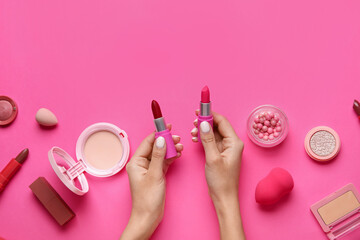 Obraz na płótnie Canvas Female hand holding lipsticks and different cosmetics on pink background