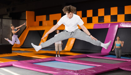 Dynamic teenage boy wearing sport clothes high jumping in trampoline arena
