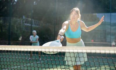 Focused positive young woman playing friendly paddleball match on outdoor summer court. Concept of sports emotions..