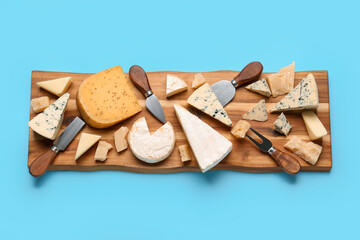 Wooden board with different types of tasty cheese on blue background