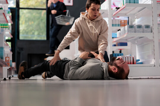 Woman helping man having foaming at mouth and convulsion during epileptic seizure in pharmacy retail store. Drugstore customer holding person having epilepsy attack, providing first aid
