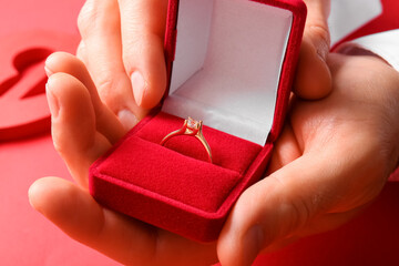 Man holding box with engagement ring on red background, closeup