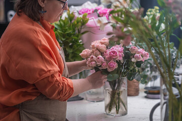 Fototapeta premium With deft hands and a keen eye for detail, the professional female florist arranges a stunning bouquet of mixed flowers