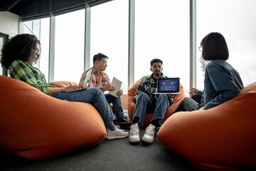 Diverse team of adults in casual clothes leveraging modern devices while working in creative office. Car designers developing digital vehicle model using computer-aided programs in meeting space.