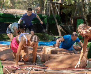 Playful sporty girl having fun competing with friends in moving through obstacle course over soft cushions in pool of water during summer weekend..