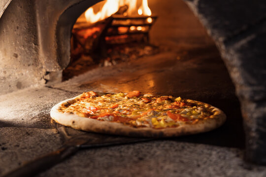 Pizza concept. Preparing traditional italian pizza. Long shovel for pizza, baking dough in a professional oven with open fire in interior of modern restaurant kitchen. High quality photo