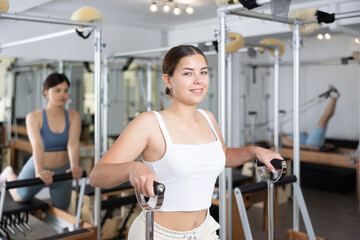 Young positive woman stretches her body muscles while sitting on a special chair in the Pilates gym