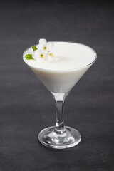 Vanilla Panna Cotta, decorated with small white flowers, in a martini glass. Dark gray background