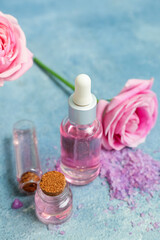 Bottles of cosmetic oil with rose extract and flowers on blue table