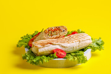 Plate of tasty shawarma with lettuce and tomatoes on yellow background