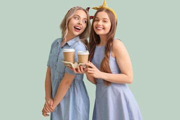 Young sisters with cups of coffee on green background