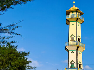 Mosque tower, green foliage and clear blue sky with negative space for text