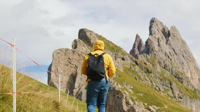 Man taking photos of Seceda mountain in Italian Alps. Male tourist with backpack uses professional camera to capture scenic landscape slow motion