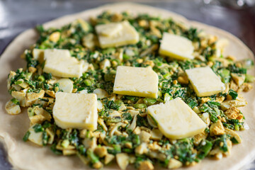 Pie with green onion and egg. Cooking a pie. Pieces of butter are on top.