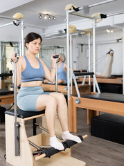 Fototapeta na wymiar Slim young woman engaging in pilates training on fitness chair in exercise room during workout session