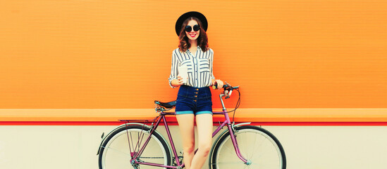 Summer image of happy smiling young woman with bicycle on orange background, blank copy space for advertising text