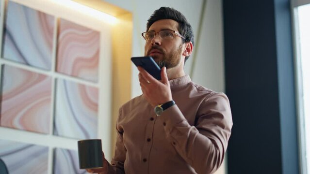 Boss recording audio message for app assistant at office holding cup close up
