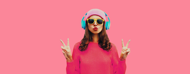 Portrait of modern young woman listening to music in wireless headphones wearing knitted sweater,...