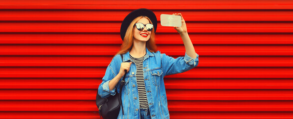 Portrait of happy smiling young woman taking selfie with smartphone wearing jean jacket, black...