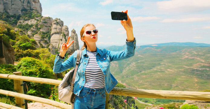 Travel concept, happy young woman taking selfie with smartphone on a hiking trail on top of the mountain Montserrat background