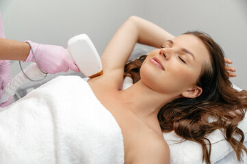 Satisfied caucasian young woman lies on the couch with protective glasses during the procedure for removing unwanted hair with a laser machine. Beauty procedure. Hair removal by laser hair removal