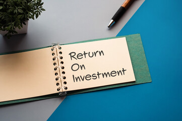 There is notebook with the word Return On Investment. It is an abbreviation for Return On Investment as eye-catching image.