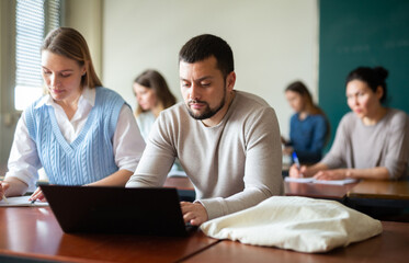 Handsome adult male student typing on laptop during lecture at university