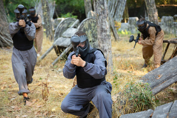 Fototapeta premium Team of happy cheerful positive smiling people playing paintball on battlefield outdoor, running with guns