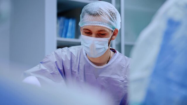 Male medic wearing mask, robe, cap and latex gloves. Patient is prepared for operation.