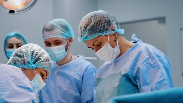 Female doctors in masks perform C-section operation. Big medical team helping new life to appear.