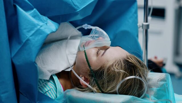 Caucasian woman with oxygen mask on the operational table. Pregnant is undergoing C-section operation.