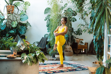 A woman practices yoga among the urban jungle. Female in yoga asanas and Pilates at home.