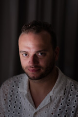 Obraz premium Posing against a dark curtain, a Middle Eastern man expresses an intense gaze directly at the camera.