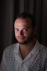Posing against a dark curtain, a Middle Eastern man expresses a conventional portrait, his head tilted slightly away from the camera.