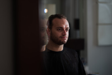 Fototapeta premium Looking at his own reflection in the mirror, a Middle Eastern man expresses a direct gaze at himself and a moment of contemplation.