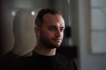 Obraz premium Looking at his own reflection in the mirror, a Middle Eastern man expresses a thoughtful portrait with his reflection repeating off into the distance behind him.