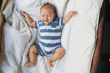A newborn baby cries on a white sheet. Childish tantrums. Colic and abdominal pain in infants. 