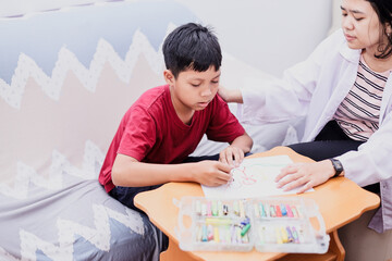 Autism awareness concept. Autism schoolboy during therapy at home with his tutor, learning to draw and having fun together.