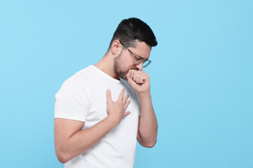 Man coughing on light blue background. Sore throat - obrazy, fototapety, plakaty