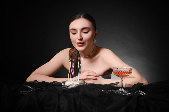Fashionable photo of attractive young woman blowing candles on her Birthday cake against black background