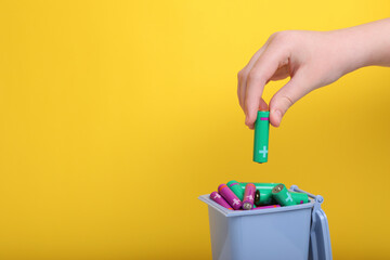 Woman putting used AA size battery into recycling bin on yellow background, closeup. Space for text