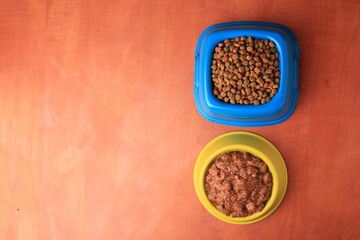 Obraz na płótnie Canvas Dry and wet pet food in feeding bowls on orange background, flat lay. Space for text