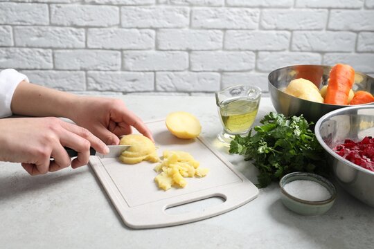 Woman cutting boiled potatoes at white table, closeup. Cooking vinaigrette salad