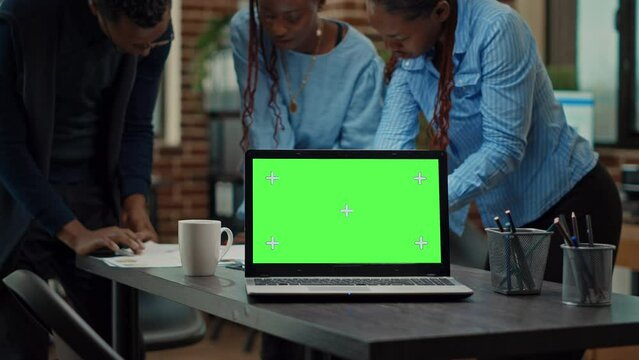 People using laptop with green screen on table, having isolated copyspace display in meeting to review annual data reports. Startup team checking papers, working with blank mockup. Tripod shot.