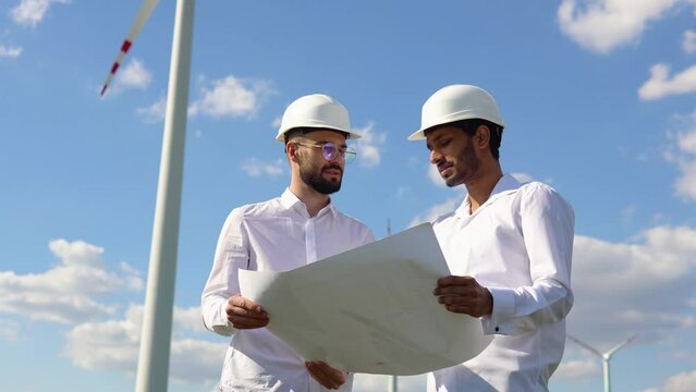 Two multiracial windmill engineers inspection and progress check wind turbine
