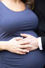 caucasian pregnant woman in blue dress with husband resting hand on her large pregnant belly