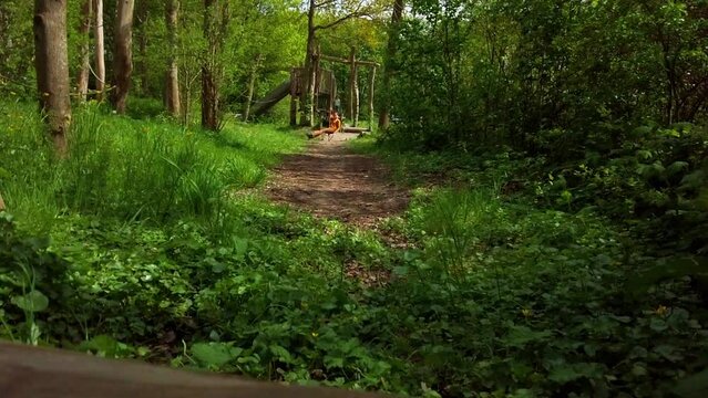 Happy nine year old girl sit on the zipline in a fresh green park. Outdoor active leisure for children who love to play in the nature playground concept. Slow motion revealing shot