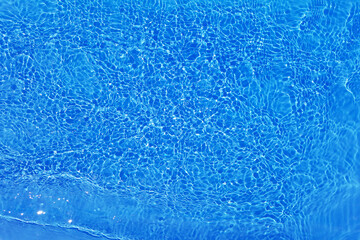 Blue water with ripples on the surface. Defocus blurred transparent blue colored clear calm water surface texture with splashes and bubbles. Water waves with shining pattern texture background.